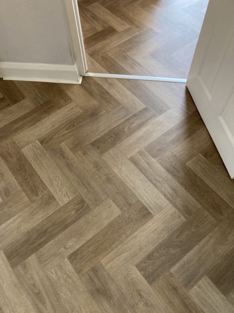 Warm wood effect herringbone vinyl flooring fitted through an interior doorway